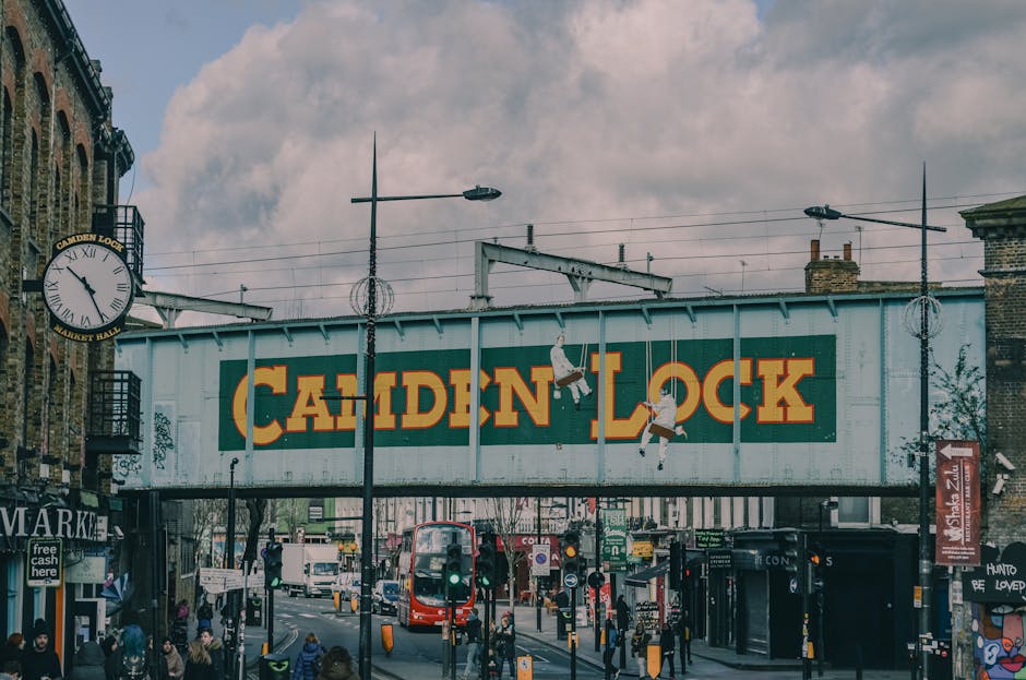 The image shows a railway bridge painted in a weathered light blue with the words 'Camden Lock' prominently displayed in bold yellow lettering. Two pairs of cartoon-style white birds with black eyes a