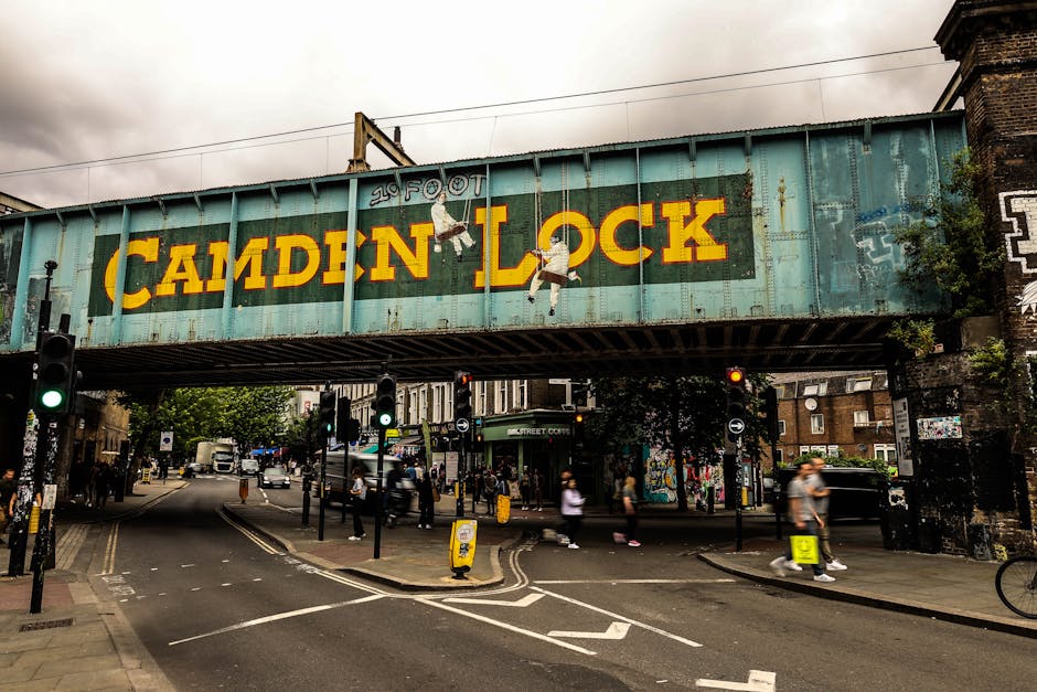 A weathered railway bridge painted in turquoise with the words 'Camden Lock' displayed prominently in bold yellow letters. The bridge features a graffiti-style logo reading '20 Foot' above the text, w